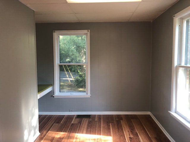 spare room with dark hardwood / wood-style floors, a drop ceiling, and wooden walls