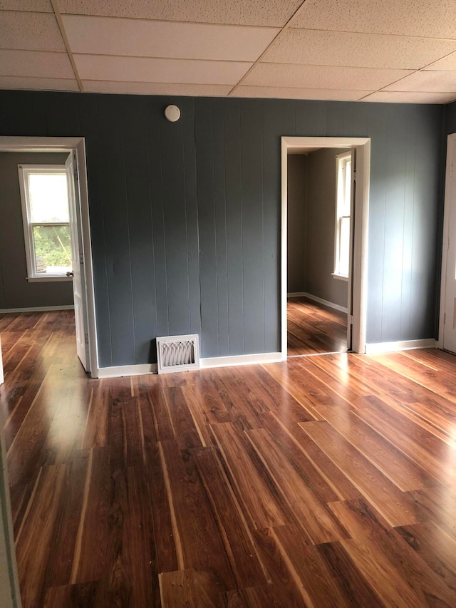 empty room with a paneled ceiling, wooden walls, and hardwood / wood-style floors