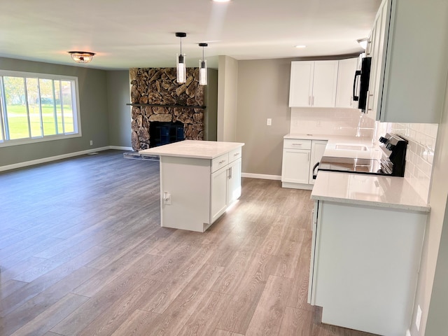 kitchen with stove, white cabinets, hanging light fixtures, and light wood-type flooring