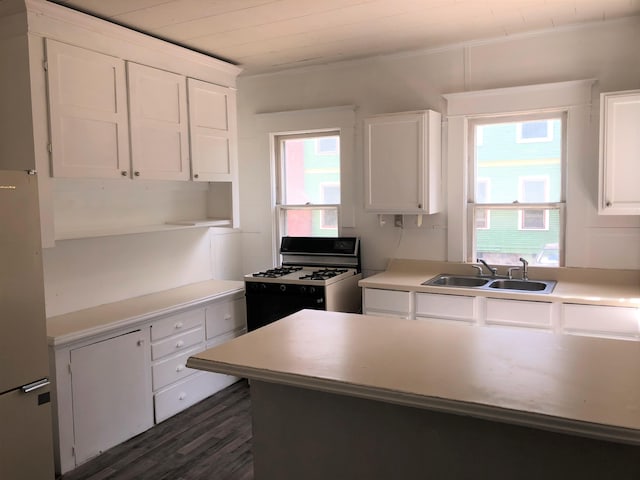 kitchen with white range with gas cooktop, a wealth of natural light, sink, and white cabinets