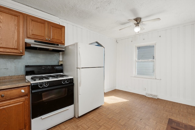 kitchen featuring a textured ceiling, white refrigerator, range with gas stovetop, ceiling fan, and light parquet flooring