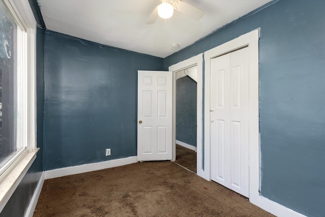 unfurnished bedroom with ceiling fan, dark carpet, and a closet