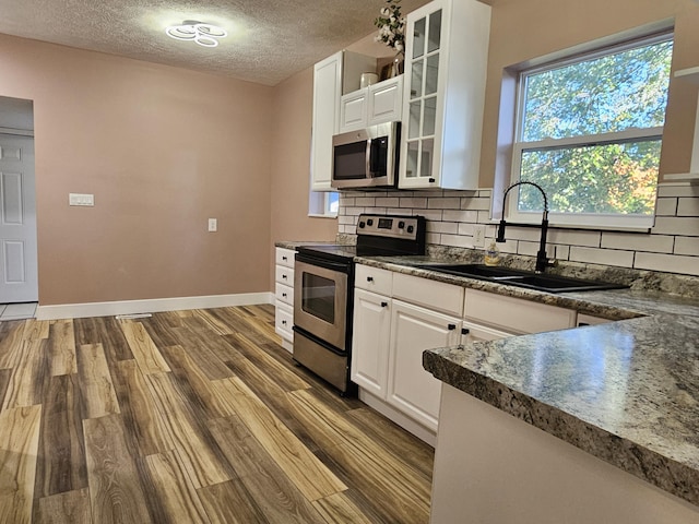 99 S Western Ave, Grant, MI 49327 - kitchen with appliances with stainless steel finishes, a sink, dark countertops, wood finished floors, and glass insert cabinets
