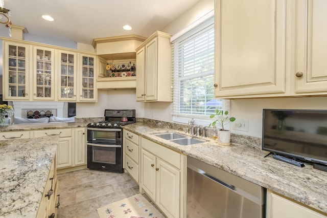 kitchen with dishwasher, sink, light stone counters, cream cabinets, and black range