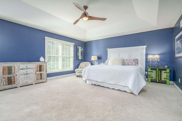 carpeted bedroom with a raised ceiling and ceiling fan