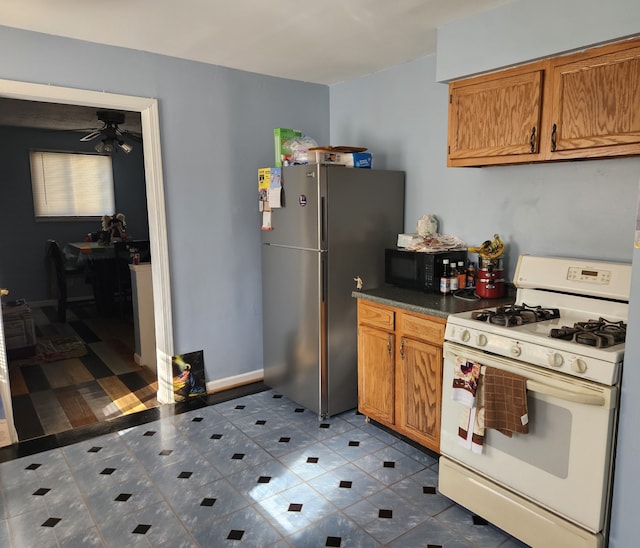 kitchen with stainless steel refrigerator, ceiling fan, white gas stove, and dark tile patterned floors