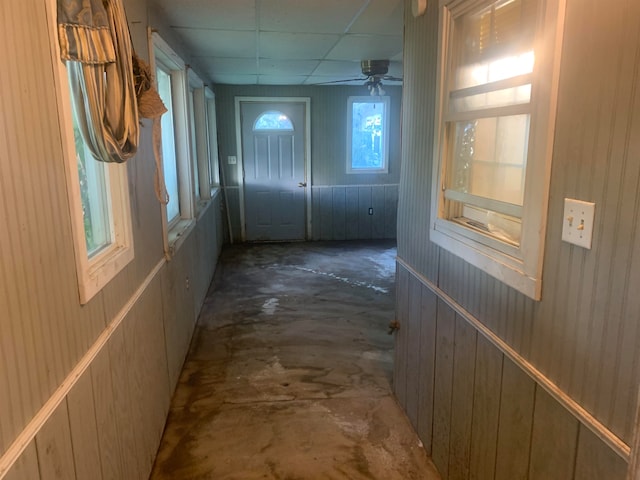 doorway featuring ceiling fan, a drop ceiling, and wooden walls