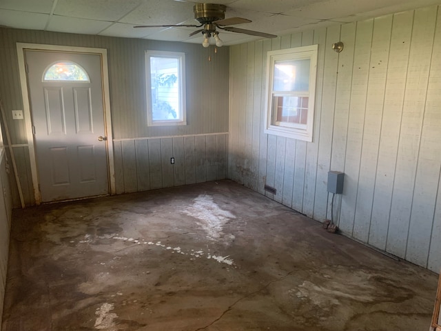 foyer featuring ceiling fan, wood walls, a drop ceiling, and concrete flooring