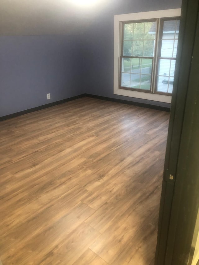 spare room featuring wood-type flooring and vaulted ceiling