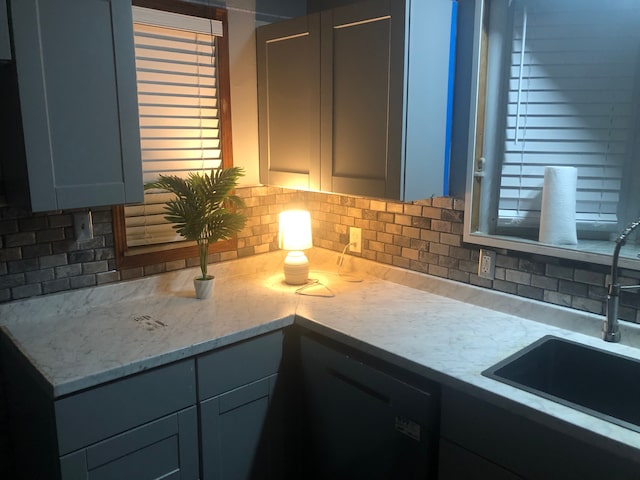 kitchen with light stone countertops, backsplash, sink, black dishwasher, and gray cabinets