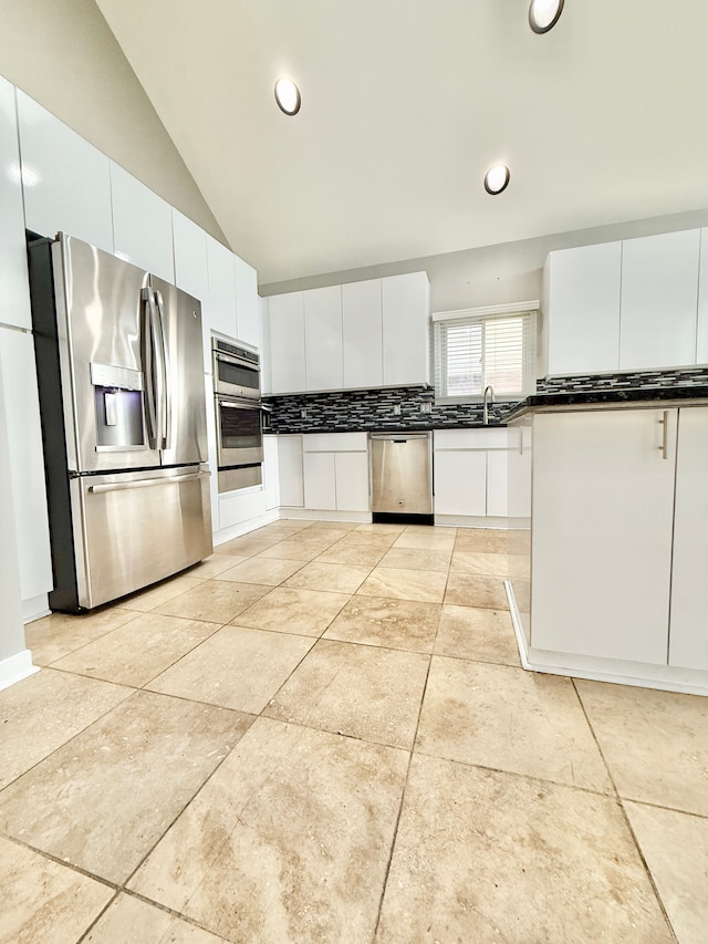 kitchen featuring tasteful backsplash, vaulted ceiling, white cabinets, and appliances with stainless steel finishes