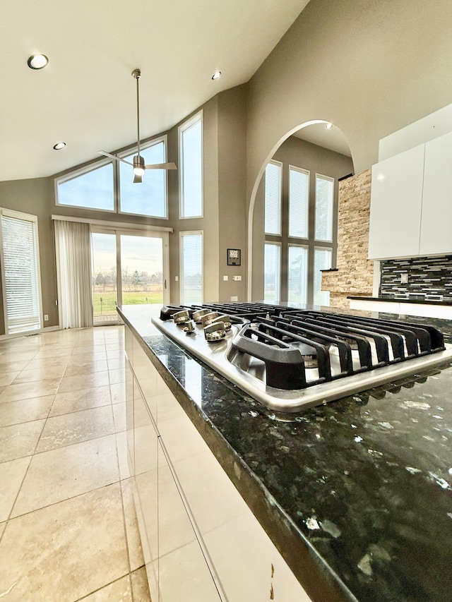 kitchen featuring light tile patterned floors, white cabinets, decorative light fixtures, dark stone counters, and stainless steel gas stovetop