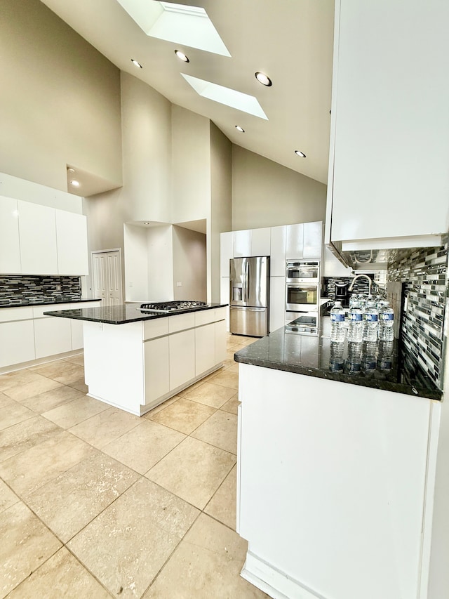 kitchen with appliances with stainless steel finishes, a skylight, white cabinetry, backsplash, and a center island