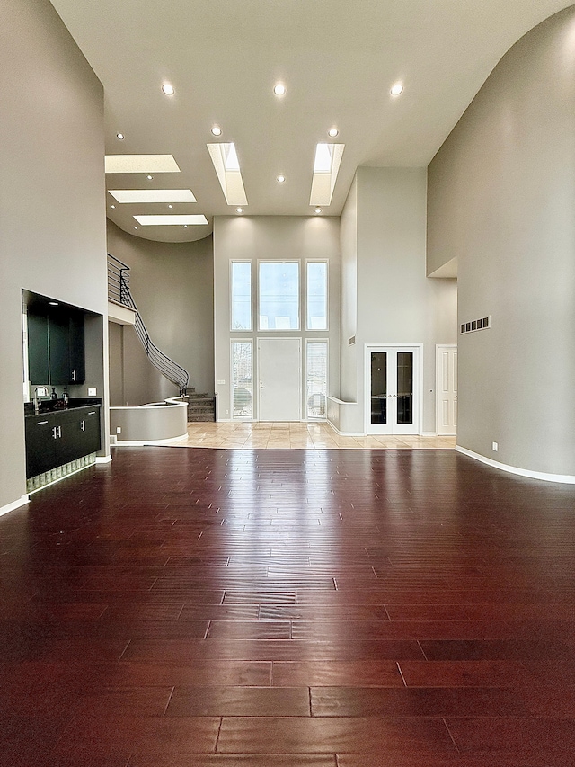 unfurnished living room with wood-type flooring, a towering ceiling, and a skylight