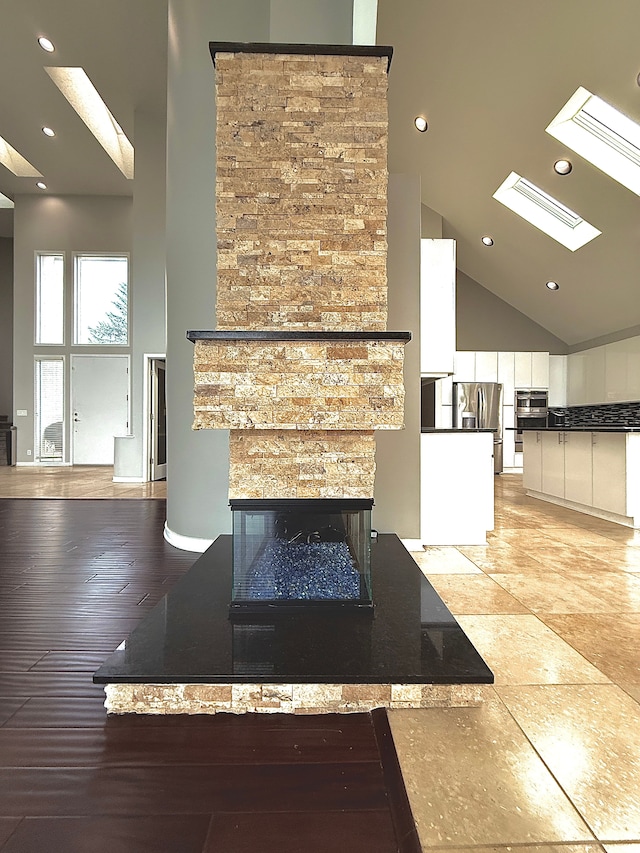 unfurnished living room featuring wood-type flooring, a fireplace, a skylight, and high vaulted ceiling