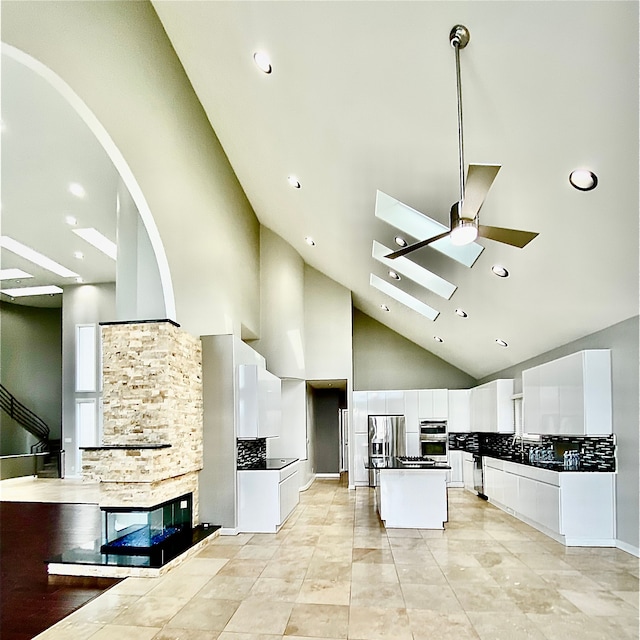 kitchen featuring high vaulted ceiling, a kitchen island, white cabinets, stainless steel appliances, and backsplash