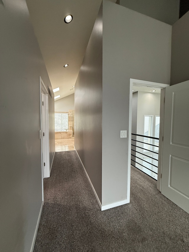 hallway with dark colored carpet and lofted ceiling