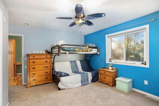 bedroom featuring a textured ceiling, light colored carpet, and ceiling fan