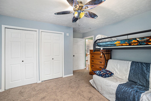 carpeted bedroom featuring a textured ceiling, ceiling fan, and multiple closets