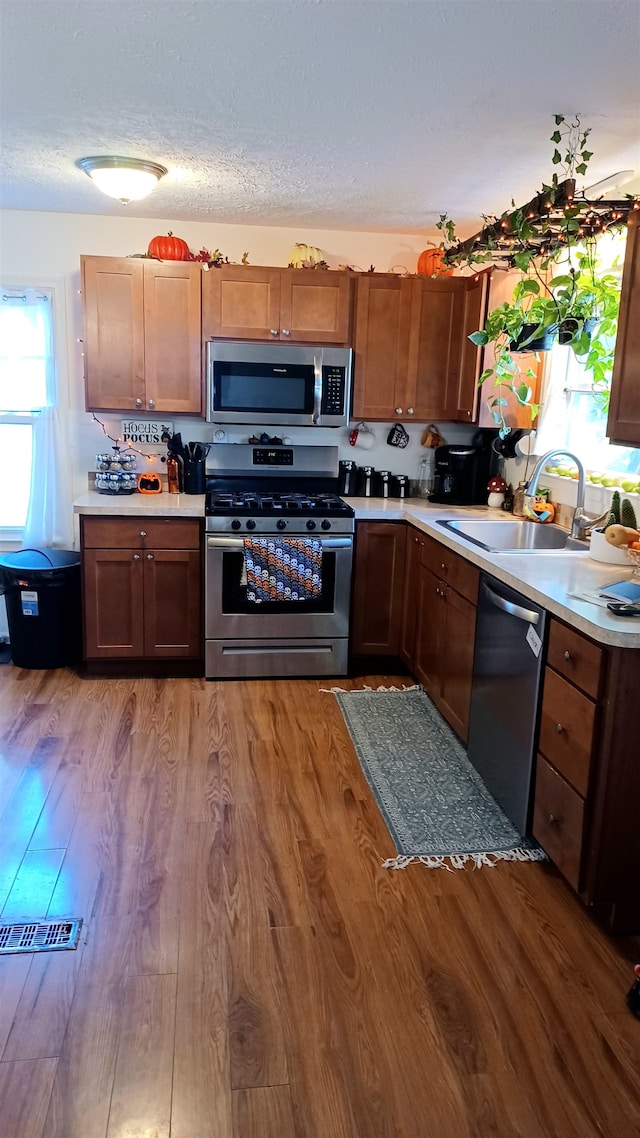 kitchen featuring wood-type flooring, a textured ceiling, stainless steel appliances, and sink