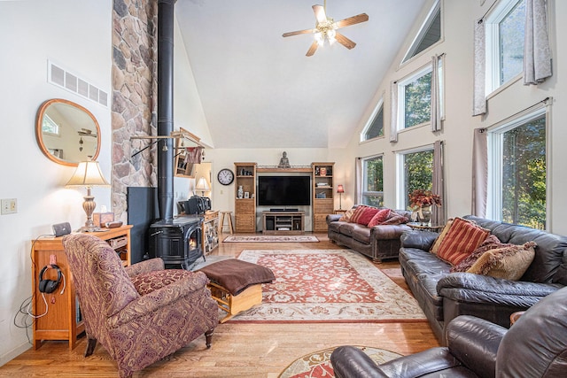 living room featuring a wood stove, ceiling fan, high vaulted ceiling, and wood-type flooring