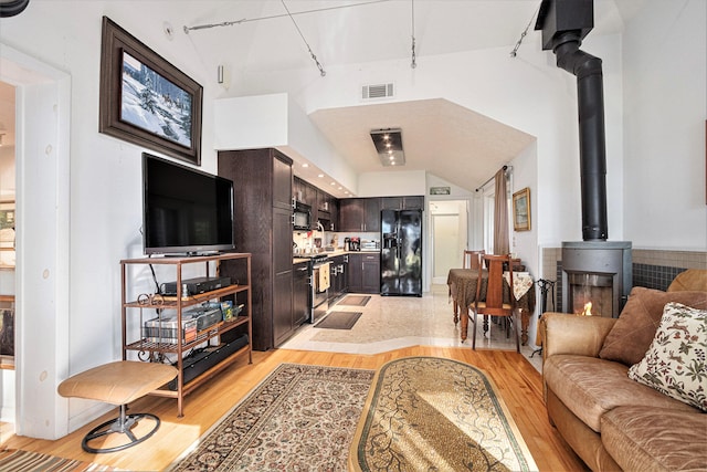 living room with a wood stove, light wood-type flooring, and high vaulted ceiling