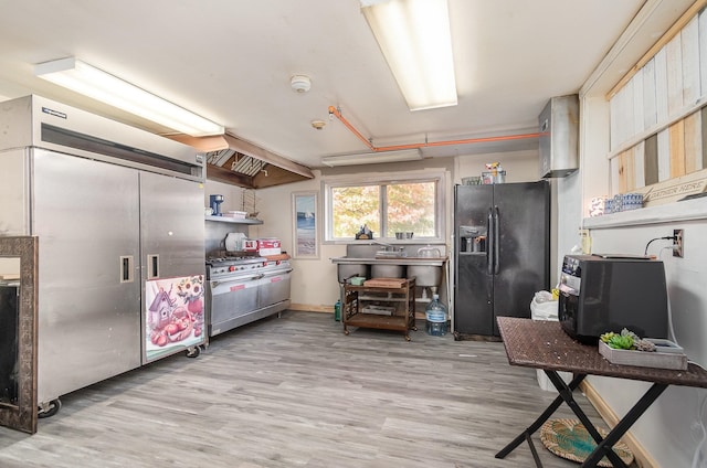 kitchen with black fridge with ice dispenser, high end stainless steel range, and light wood-type flooring