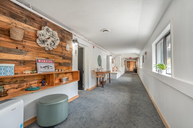 corridor with wood walls, carpet floors, and a textured ceiling