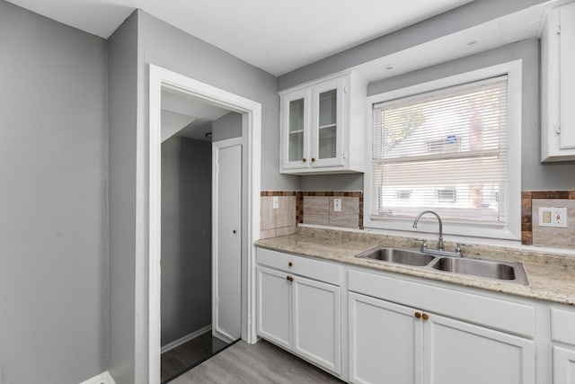 kitchen with decorative backsplash, white cabinetry, sink, and light wood-type flooring