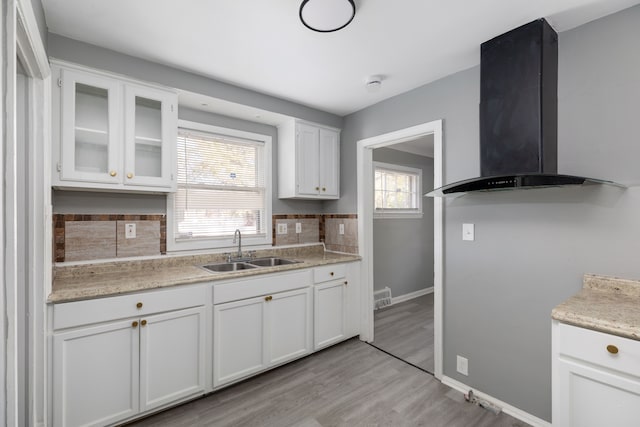 kitchen featuring white cabinets, wall chimney range hood, sink, decorative backsplash, and light wood-type flooring