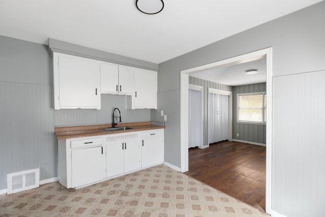 kitchen with light hardwood / wood-style floors, white cabinetry, sink, and wooden walls