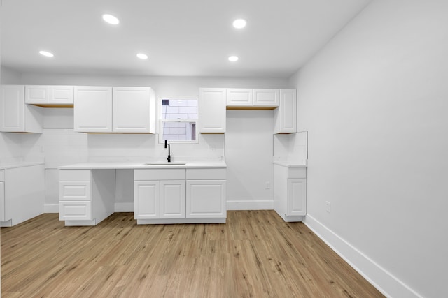 kitchen featuring backsplash, white cabinetry, sink, and light wood-type flooring