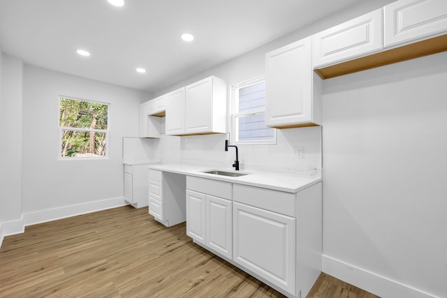 kitchen featuring white cabinets, decorative backsplash, light wood-type flooring, and sink