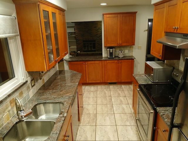 kitchen with sink, stainless steel appliances, a brick fireplace, dark stone countertops, and decorative backsplash