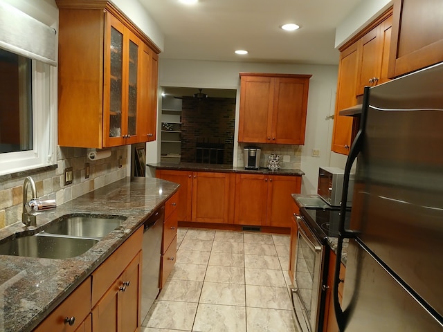 kitchen featuring appliances with stainless steel finishes, tasteful backsplash, sink, dark stone countertops, and light tile patterned flooring