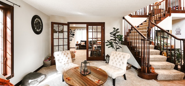 sitting room featuring french doors, a textured ceiling, and light colored carpet