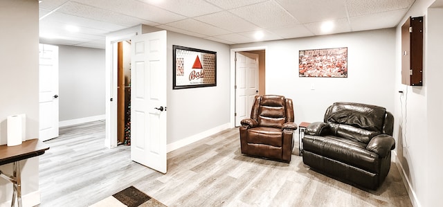 living area with a paneled ceiling, electric panel, and light hardwood / wood-style flooring