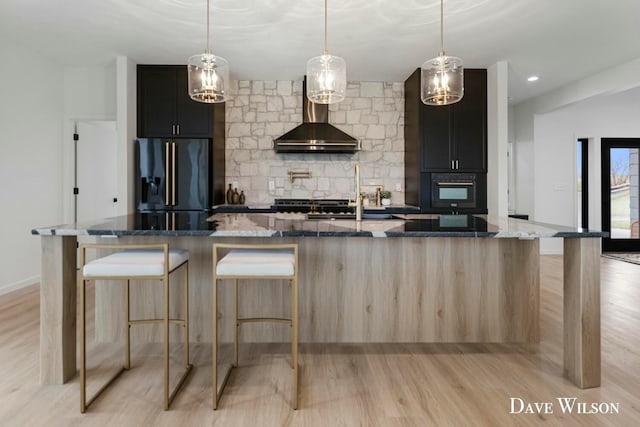 kitchen with appliances with stainless steel finishes, light wood-type flooring, dark stone counters, hanging light fixtures, and a large island