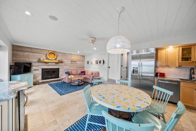 dining area featuring stone tile floors, a ceiling fan, recessed lighting, ornamental molding, and a stone fireplace