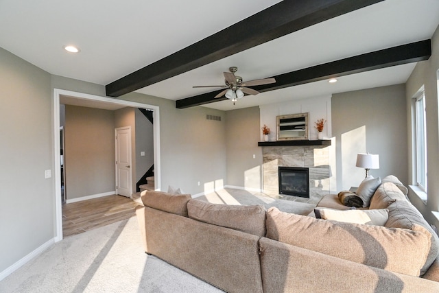 living room with beam ceiling, a tile fireplace, ceiling fan, and light hardwood / wood-style floors