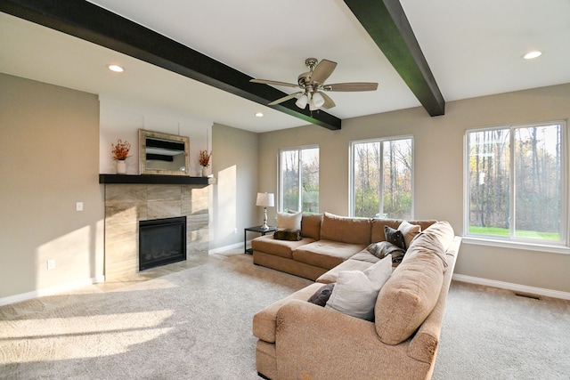 living room featuring beamed ceiling, ceiling fan, light carpet, and a tile fireplace