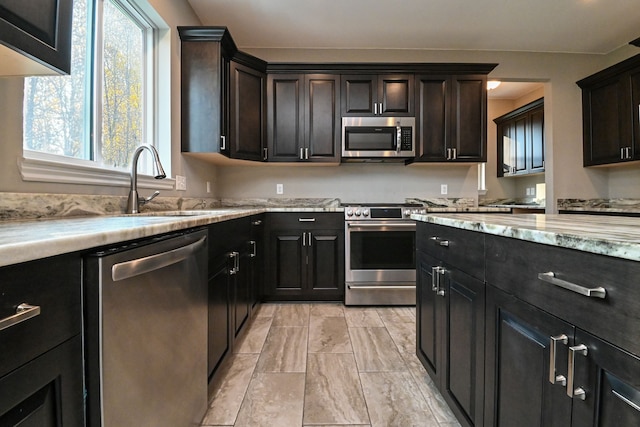 kitchen featuring appliances with stainless steel finishes, dark brown cabinetry, light stone counters, and sink