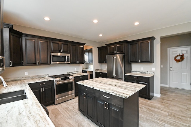 kitchen with light stone counters, stainless steel appliances, sink, light hardwood / wood-style flooring, and a center island