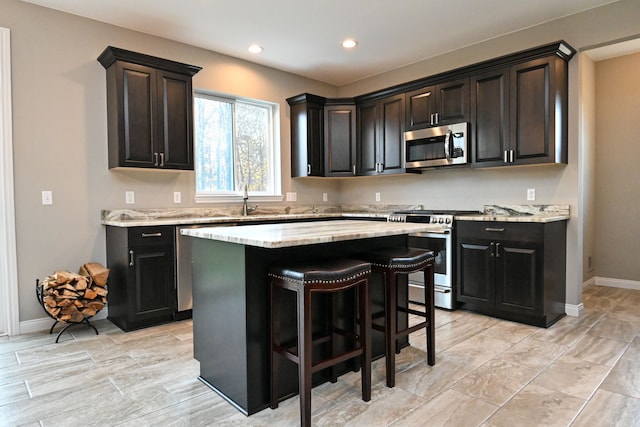 kitchen featuring light stone countertops, sink, stainless steel appliances, a breakfast bar, and a kitchen island