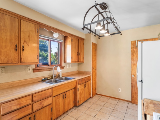 kitchen featuring light tile patterned flooring, white refrigerator, hanging light fixtures, and sink