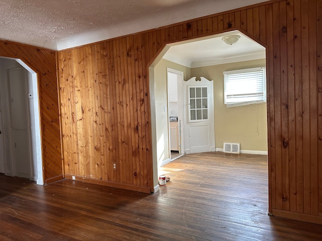 empty room featuring a textured ceiling, dark hardwood / wood-style flooring, crown molding, and wood walls