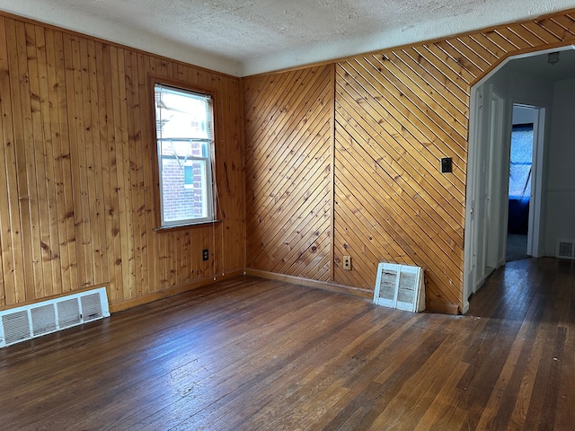 spare room featuring wooden walls, dark wood-type flooring, and a textured ceiling