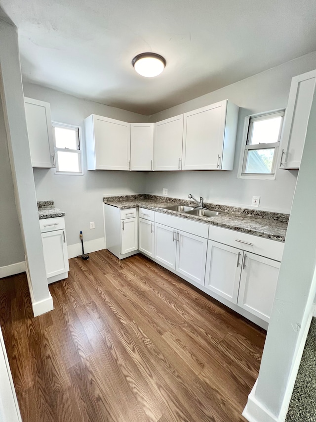 kitchen with dark stone counters, sink, white cabinets, and hardwood / wood-style floors