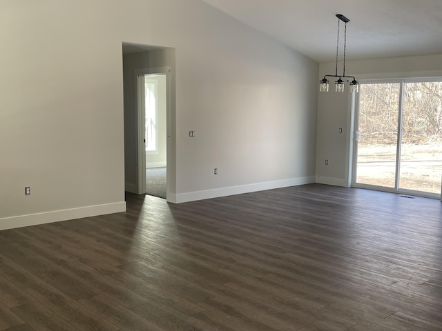 spare room featuring dark wood-style floors, a notable chandelier, baseboards, and vaulted ceiling