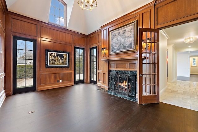 unfurnished living room featuring a premium fireplace, a towering ceiling, dark wood-style floors, an inviting chandelier, and crown molding